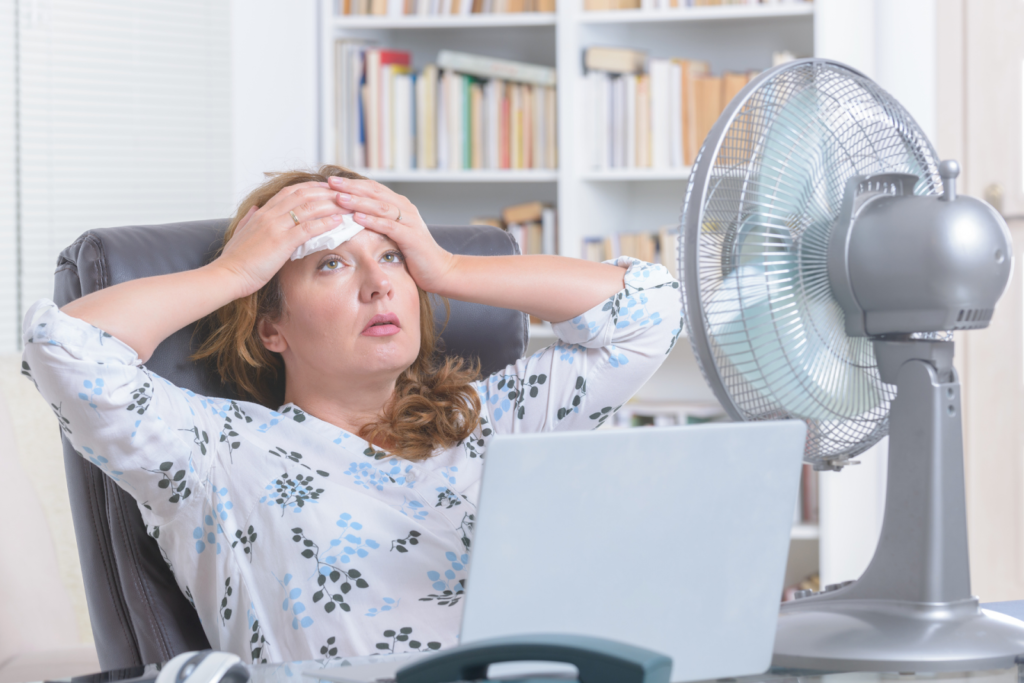 sweaty woman cooling down with fan because of broken ac