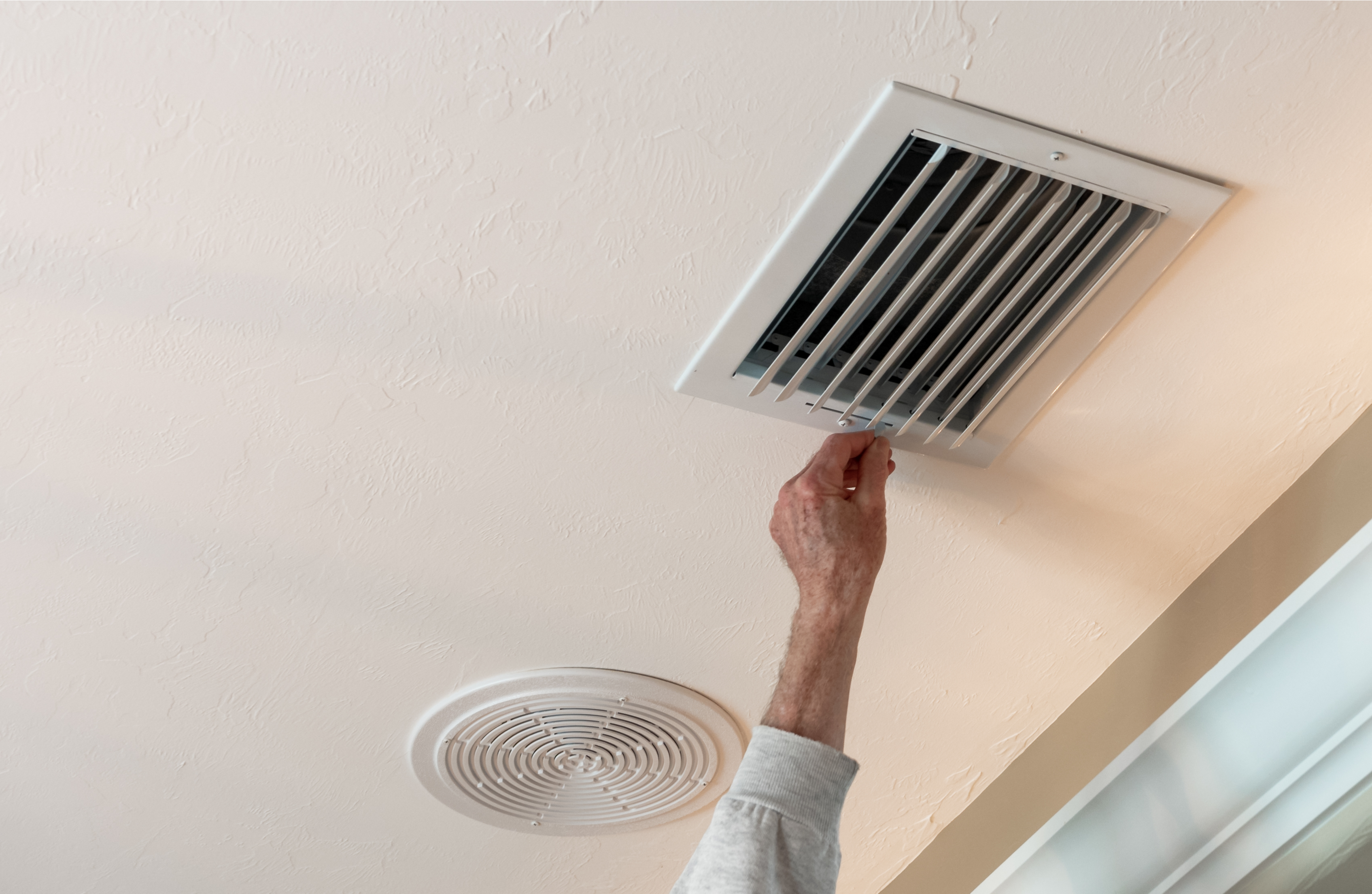 Homeowner in New Orleans closing vent in ceiling for temperature control.