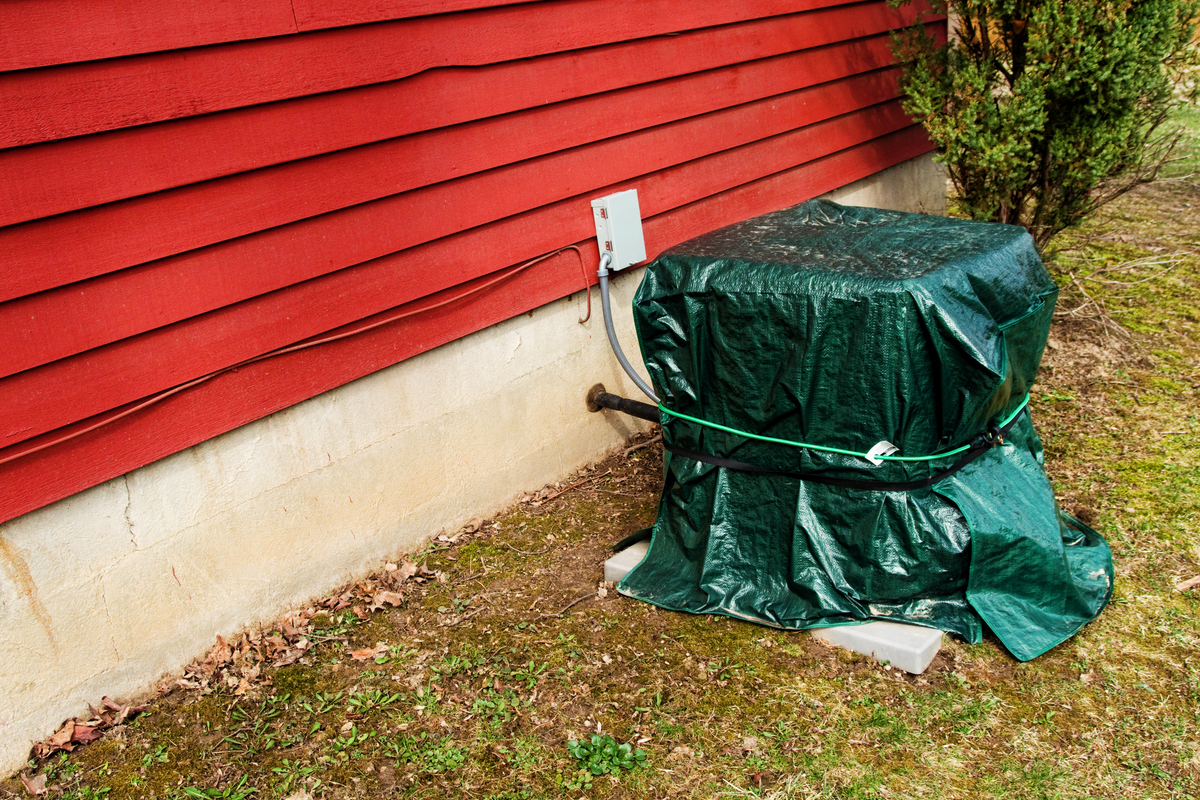 Outdoor AC unit covered with tarp and rope to protect against high winds and flying debris during hurricane season.