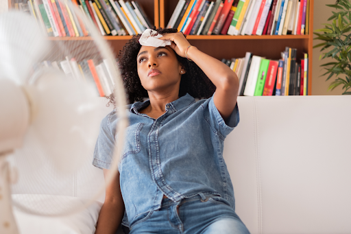 Homeowner sitting on couch with fan blowing on her due to broken AC blowing warm air.