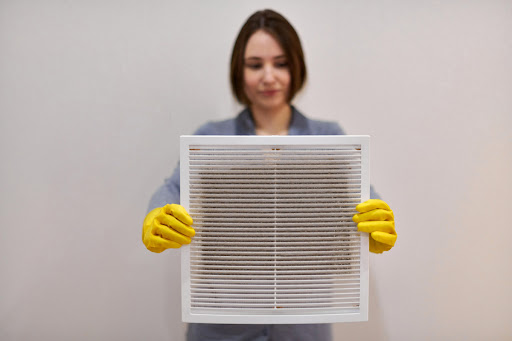 A woman wearing yellow gloves holding a dirty HVAC air filter.