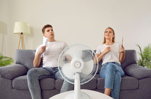 A man and woman sitting on a couch in front of a man with paper fans in their hands.