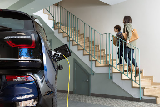 A woman and child walking up basement steps while an electric vehicle charges in the basement.