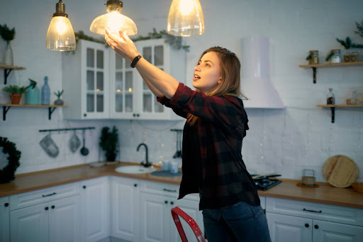 A woman changing a light bulb in a house.