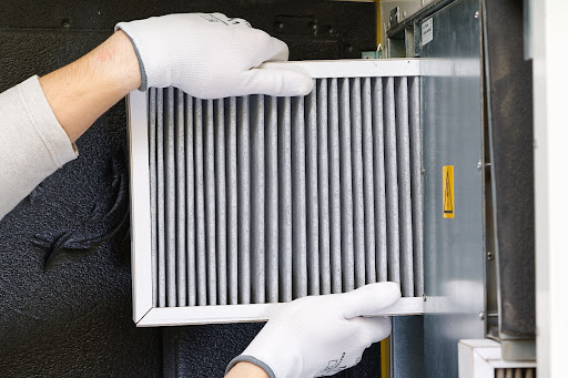 A close up of gloved hands replacing a furnace filter.