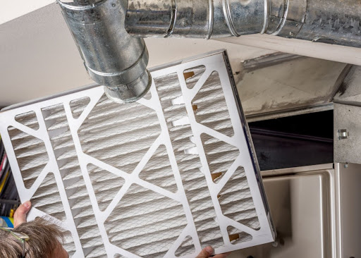 A man installing a new furnace air filter during furnace maintenance.