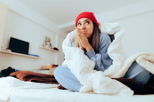 A woman in bed wrapped in a blanket due to a cold home.