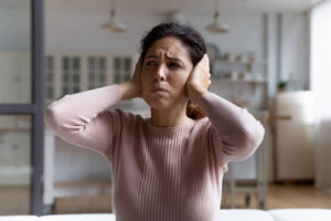 A woman covering her ears due to a loud noise in her home.